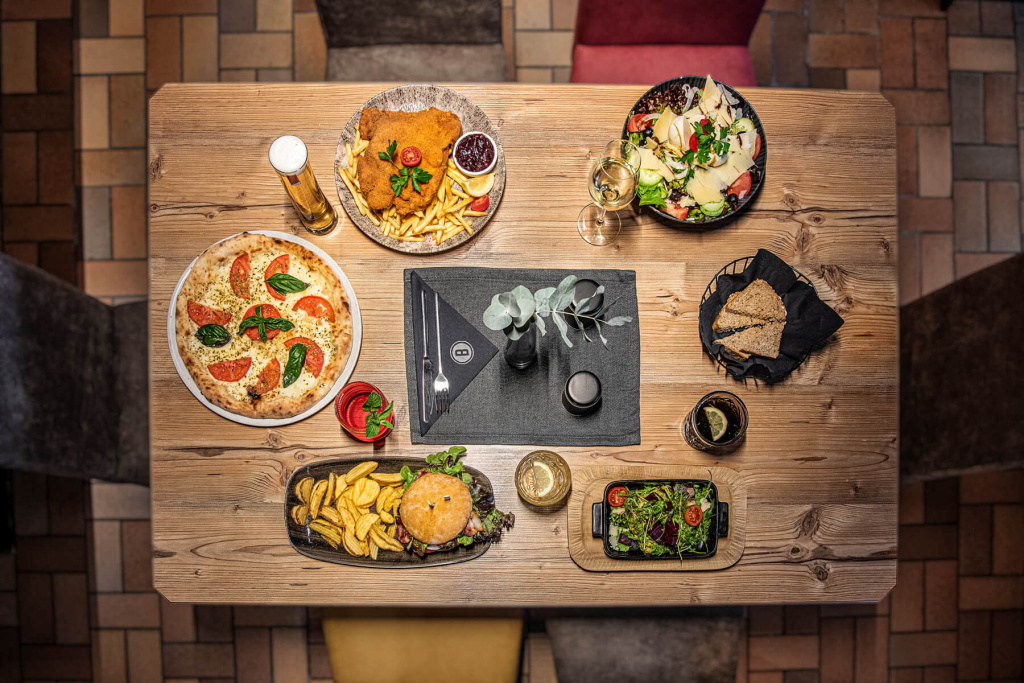 Holzofenpizza, Schnitzel, Burger und Salat auf Holztisch im Restaurant Bad Hofgastein